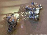 Two metal wall sculptures on wall, each shaped as stylized female torsos made of circular washers