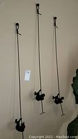 Three black metal wall sculptures showing figures climbing twisted rods, hanging on a wall.