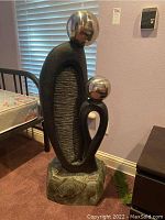 Full front view showing tall black and gray resin fountain sculpture with two reflective metal spheres at the top and rock-textured base