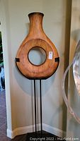 Full view of the wooden circular art sculpture mounted on a black metal stand, showing its overall shape and condition.
