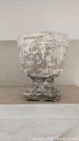 White and brown weathered cement planter with pedestal base exhibiting rustic patina.