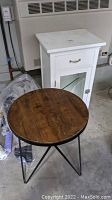 Round wooden top side table with black metal frame base, showing signs of wear and dust.