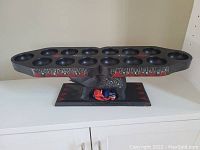 Side view of the Congkak board showing holes, elephant figure stand, red and black painted details, and cloth bag of stones inside elephant space.