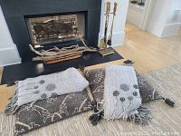 View of fireplace area showing fireplace tools stand with tools, basket containing driftwood, and two folded blankets in front on rug.