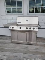 Front view of stainless steel Virco The Classic propane grill showing five control knobs, storage cabinet with double doors, and large lid
