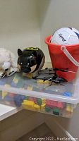 Shelf with white stuffed dog, clear container with colorful blocks, black cat piggy bank, toy police helicopter, white soccer ball in red bucket