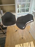 Pair of mid-century modern style plastic shell chairs with black and white houndstooth upholstery and metal wire Eiffel style bases in an office setting near windows.
