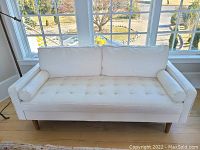 Front view of the white leather-like sofa showing tufted seat and rolled end pillows.