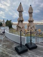 Three beige outdoor patio umbrellas closed and standing on a deck with black weighted bases.