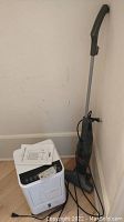 Proaller portable air conditioner alongside Bissell stick vacuum against corner wall.