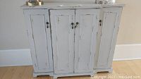 Full frontal view of the weathered gray sideboard with four cabinet doors, showcasing the distressed paint finish and drop pull handles.