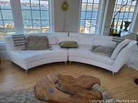 Full view of two-piece curved white leather sectional sofa in room with waterfront view