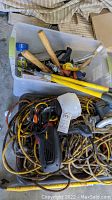 Overview photo of multiple tools including power saw, extension cords, tools with wooden handles inside plastic tubs