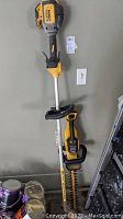 Photo showing DeWalt weed trimmer and hedge trimmer side by side, both cordless with yellow and black bodies, wall background.