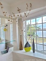 Three unique tall decorative vases on a white window ledge: one tall textured brown wood-patterned vase, one round black and yellow vase with branches, and one tall golden-brown vase with branches.