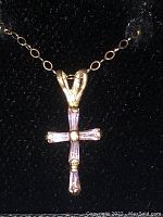 Close-up image of 14kt gold chain with pink gem cross pendant showing the front side of the cross against a black velvet background.