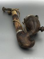 Side angle of the antique capped pipe showing large wooden bowl with hinged metal cap and irregular textured stem with attached small wooden elements and string.