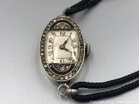 Close-up image of the oval watch face showing marcasite stones around bezel, Art Deco styled dial with black numerals and blue hands