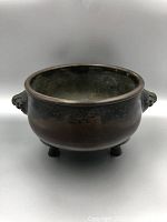 Front view of bronze tripod censer showing round body, patina and handles