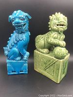Front view of two Foo Dog porcelain statues, blue and green, showing facial and base details.