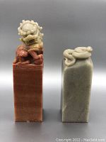 Front view of the two Chinese stone seals, one reddish with lion carving and one grey-green with coiled serpent carving