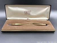 Gold filled mechanical pencil in rectangular box with tan velvet holding surface and satin interior imprinted with 'CROSS SINCE 1846'. Pencil is ridged with clip and eraser ends visible.