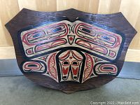 Front view of the double headed sea monster wooden plaque with bold geometric patterns in black and red on a brown wood background.