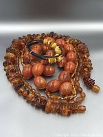 Five amber jewelry pieces arranged on gray background: chip necklace, oval bead necklace, round bead necklace, disc bead necklace, coil bracelet