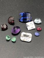 Photo showing ten loose faceted gemstones in various colors including green, red, purple, blue, and clear white on a black background.