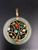 Front view of circular jade ring pendant showing twisted gold wire tree with multi-colored gemstones and pearls attached.
