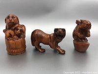 Three wooden netsuke carvings of a dog with puppies, tiger, and rabbit displayed side by side
