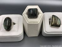 Photo showing the three labradorite rings mounted on white displays, highlighting their shapes and metal settings.
