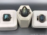 Three vintage labradorite cabochon rings displayed on white stands showing the stone shapes and metal settings.