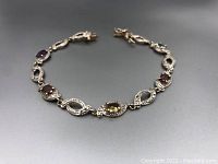 Full view of tennis bracelet laid out showing alternating gemstone and infinity-shaped linked sections.