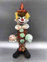 Front view of Murano glass clown with multicolored swirled body, yellow hair, red nose, holding crystal sphere