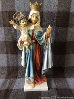 Front view of the religious statue depicting Mary with baby Jesus, showing detailed facial features, crown, robes and rosary beads.