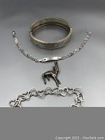 Overall view showing three bracelets and animal pendant arranged on gray surface.