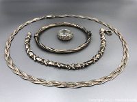 Full lot of four sterling silver jewelry pieces on gray background: necklace, two bracelets, and ring.