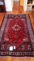 Full view of rectangular red rug with central medallion and border patterns laid on wood floor