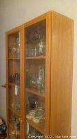 Front side view of tall wooden display cabinet with glass doors.