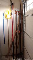 Two 6-foot pipe clamps, a red-handled digging bar, a mop handle, and additional tools standing against a wall