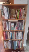 Full view of wooden shelving unit on hardwood floor, filled with cookbooks on three shelves