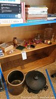 Books on top shelf with small decorative items on the middle shelf including a ceramic crock and cast iron pot on floor level