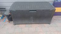 Full front view of dark brown plastic deck storage box with woven texture and curved lid, standing on patio