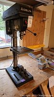 Delta 11-990 drill press standing on a workbench, showing work table and base