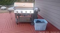 Weber Genesis II GS4 grill on deck with side tables and plastic tub of accessories at right
