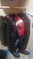 Photo showing three hanging items: a red and black Joe Rocket armored motorcycle jacket, a black leather jacket, and a black leather vest, all hung on hangers.