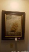 Framed ship painting hanging on a wall showing the entire artwork and frame.