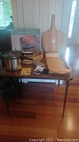 Full lot overview on folding table showing all items including manual freezer defroster box, Presto pressure cooker, wooden tray and cutting board, chip and dip dish and basket.
