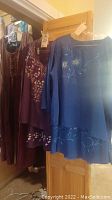 Blue silk hand-painted skirt and blouse set and purple Renaissance dress hung on wooden door and wall showing overall condition and style.